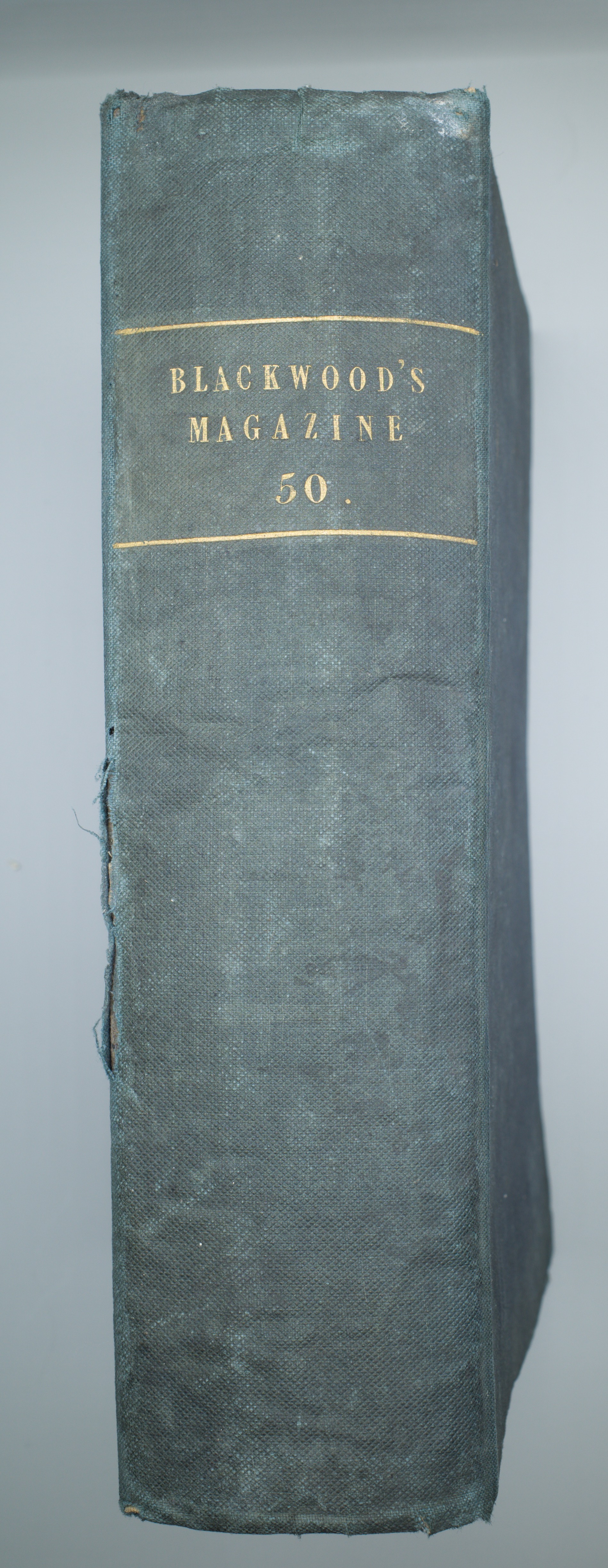 Upright spine of a blue cloth-bound volume labelled Blackwood’s Magazine 50 in gold lettering, with frayed cloth at the edges.